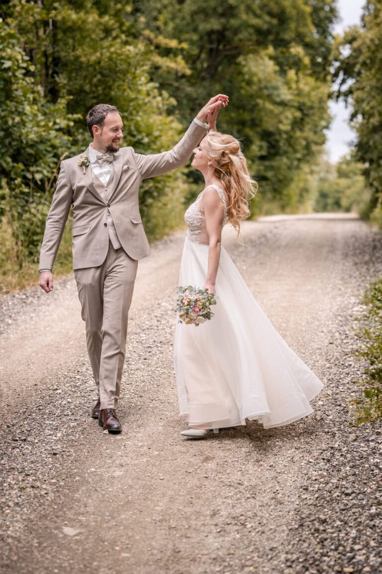 Brautpaar tanzt lachend auf einem Waldweg bei ihrer Hochzeit in Kühbach