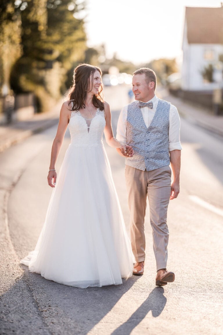 Brautpaar bei kirchlicher Hochzeit in Dasing läuft auf der Straße beim Sonnenuntergang dem Fotografen entgegen