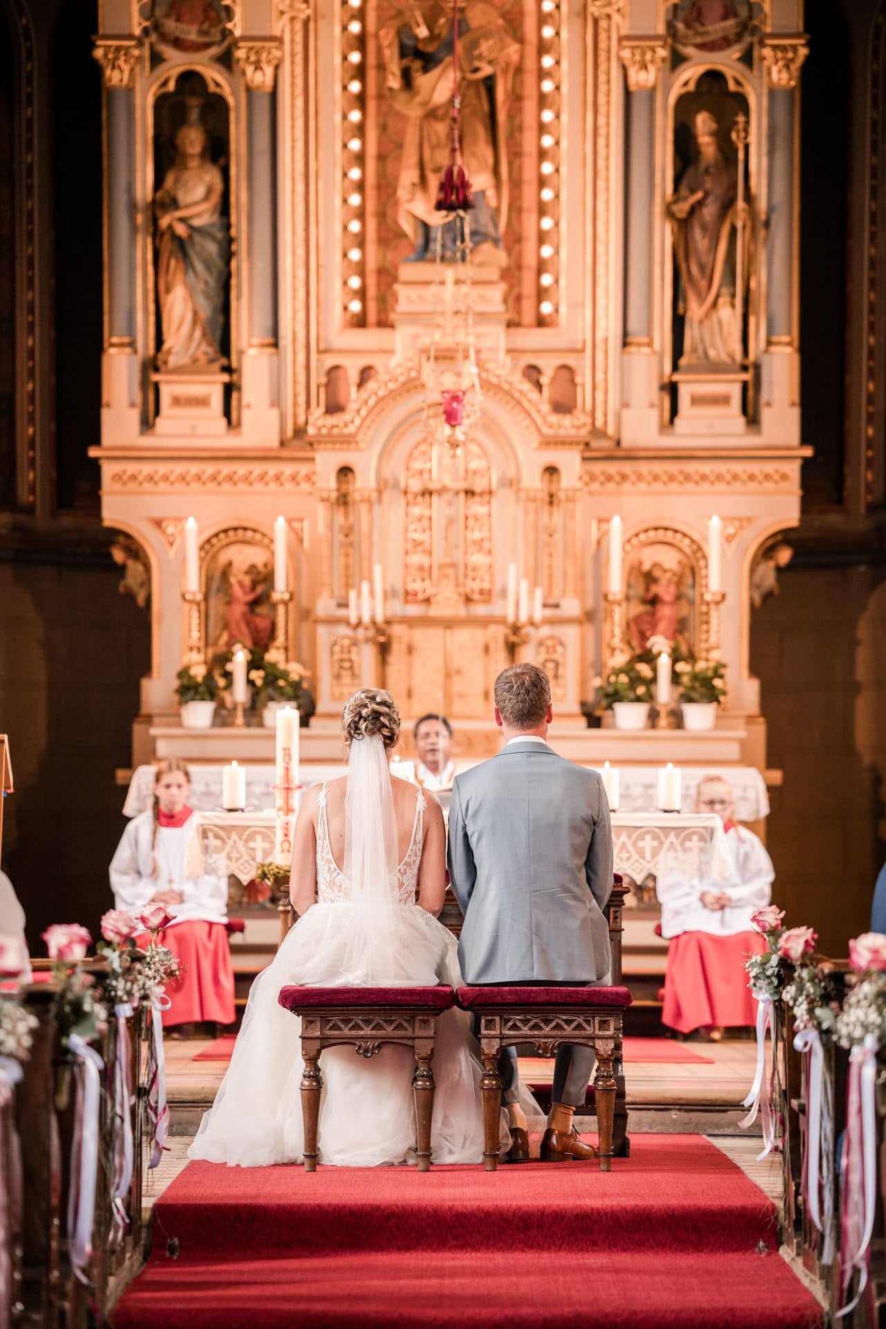 Brautpaar sitzt während der kirchlichen Trauung in einer festlich geschmückten Kirche in Augsburg vor dem Altar