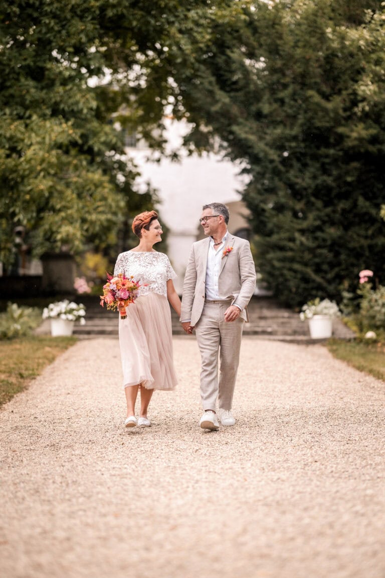 Brautpaar spaziert Hand in Hand über eine Kiesallee bei ihrer Hochzeit in Kühbach